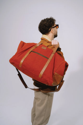 Burgundy travel duffel bag worn over the shoulder while standing