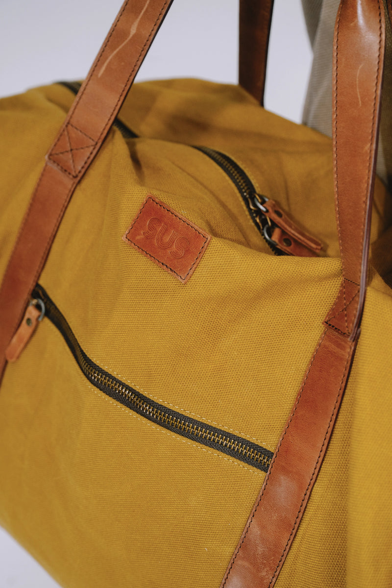 Close-up of leather straps and stitching on ochre travel duffel bag