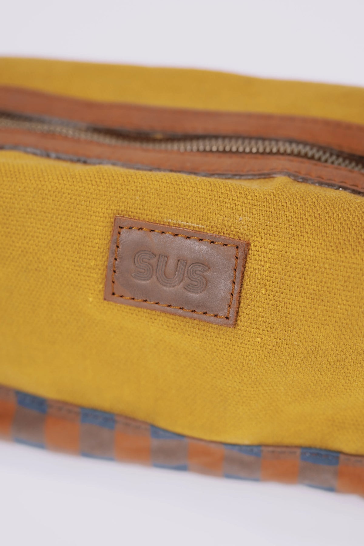 Close-up of a SUS logo on a golden ochre toiletry bag