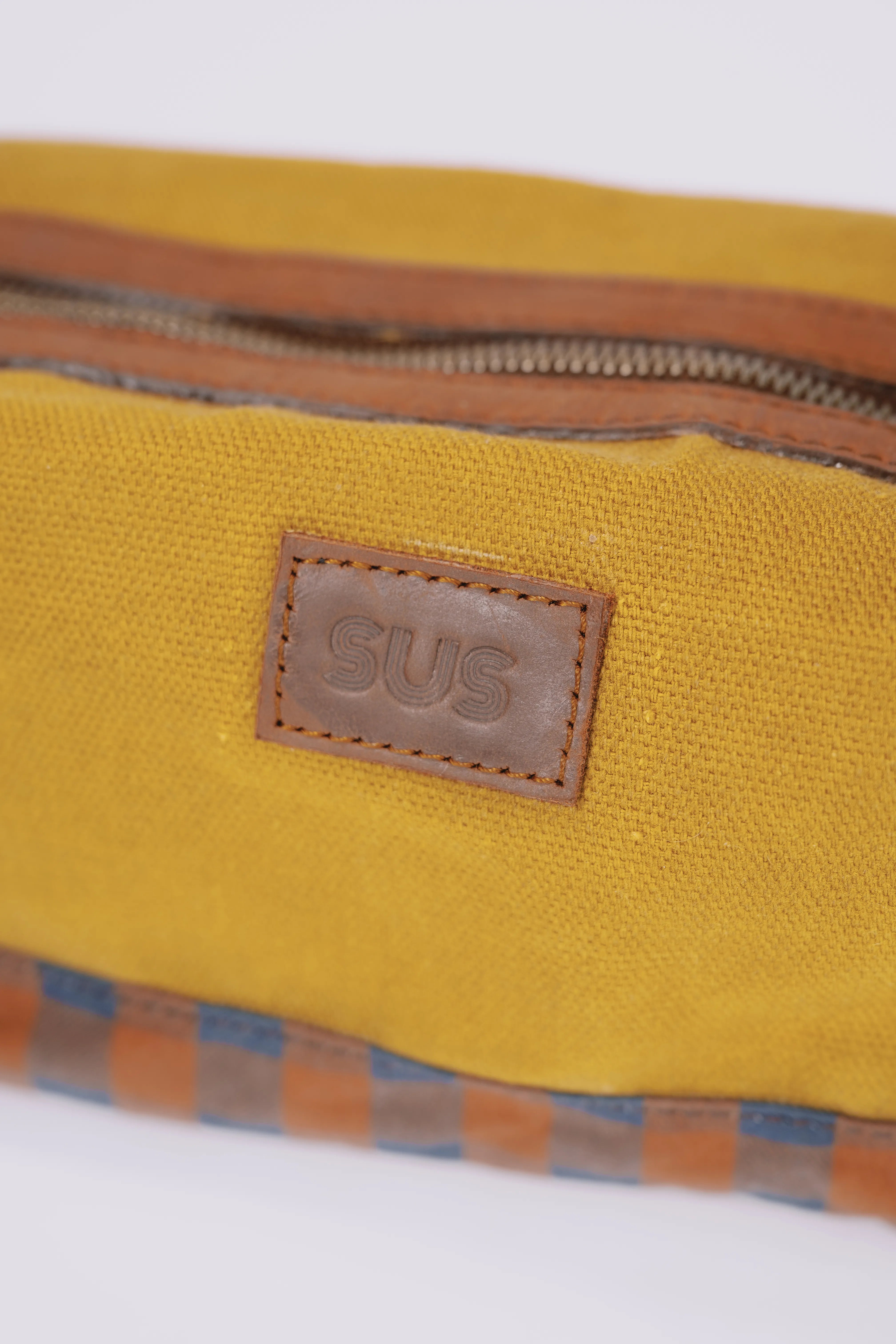 Close-up of a SUS logo on a golden ochre toiletry bag
